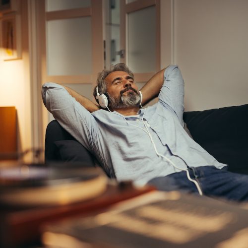 mid aged man listening music with headphones on phonograph, relaxed in sofa at his home